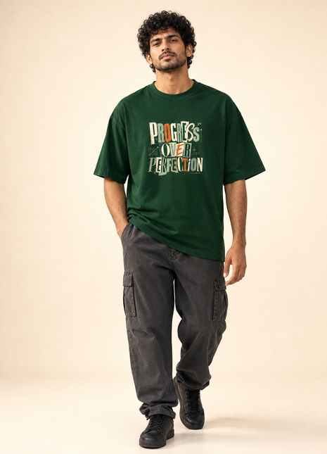 Indian male model in PAXBURY Progress Over Perfection bottle green UC22 loose unisex T-shirt, large cream sage rust front typography