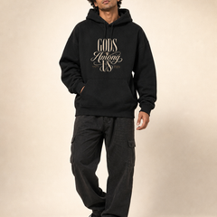 Indian male model wearing PAXBURY Gods Among Us black unisex UH32 hoodie with original-style cream GODS Among US typography centred above front pouch