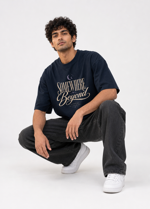 Indian male model crouching wearing PAXBURY Somewhere Beyond navy relaxed UC22 graphic T-shirt with cream typographic front print