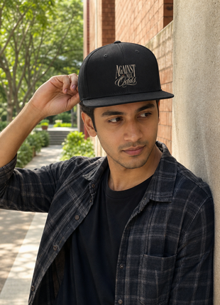 Indian male model leaning near campus wearing PAXBURY Against All Odds black snapback cap