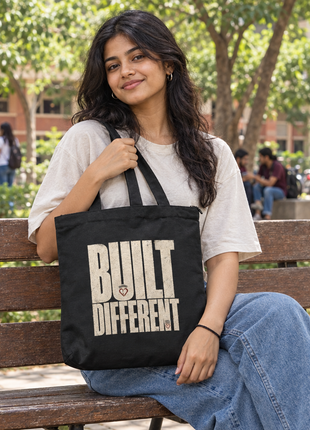 Built Different black zippered tote, original bold typography front, Indian college student seated on campus bench