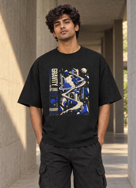Indian male wearing Gravity Is Optional black oversized T-shirt with blue-and-gold orbital graphic and vertical front lettering