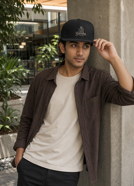 Indian man leaning outside an office wearing The Last Guardian black cotton snapback cap
