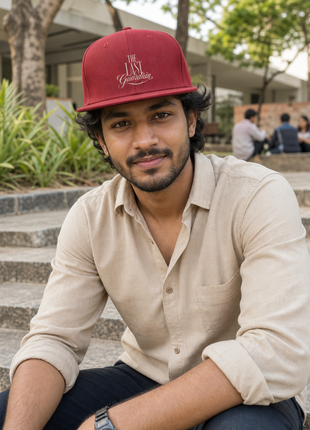 Indian man seated on college campus steps wearing The Last Guardian red cotton snapback cap
