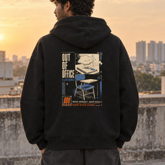 Indian male model wearing black Out of Office oversized hoodie with travel scene, folding chair and OUT OF OFFICE back artwork