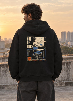 Indian male model wearing black Out of Office oversized hoodie with travel scene, folding chair and OUT OF OFFICE back artwork
