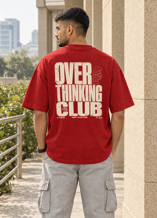 Same male model from front view photographed from behind in Kittl; large distressed cream OVER THINKING CLUB back graphic on red PAXBURY tee