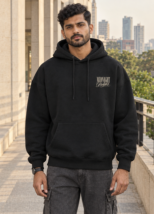 Kittl Indian male model front wearing PAXBURY Midnight Predator black UH32 oversized hoodie with small cream left chest Midnight Predator text