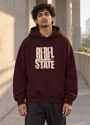 Indian male model wearing PAXBURY Rebel State maroon oversized hoodie, bold cream REBEL STATE chest print