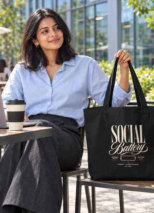 Social Battery large black tote script front — Indian office-going woman seated outside glass office café