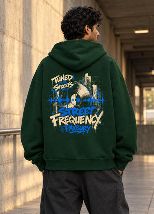 Indian male model wearing Street Frequency bottle green oversized hoodie with vinyl-record and electric-blue city artwork on back