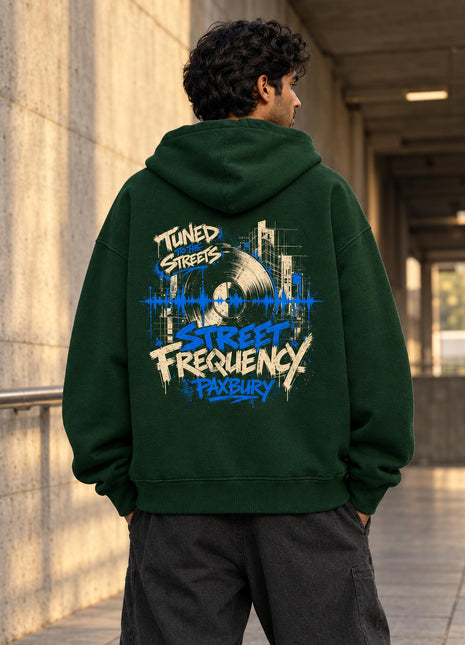 Indian male model wearing Street Frequency bottle green oversized hoodie with vinyl-record and electric-blue city artwork on back