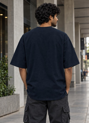 Plain back view on Indian male model of navy oversized The Last Guardian UC22 T-shirt