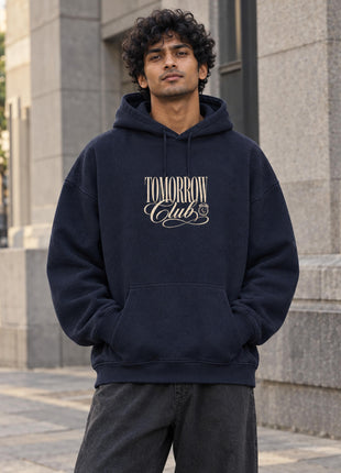 Indian male wearing Tomorrow Club navy oversized hoodie with cream vintage TOMORROW Club chest lettering