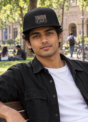 Black PAXBURY Tomorrow Club snapback cap worn by Indian male student seated on university bench