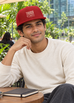 Red PAXBURY Tomorrow Club flat-visor snapback, Indian male young professional seated at outdoor office café